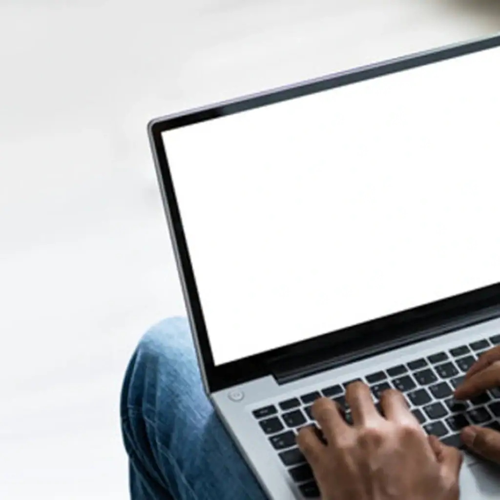 Eine Person hat einen offenen Laptop auf dem Schoß, die Finger tippen auf der Tastatur.