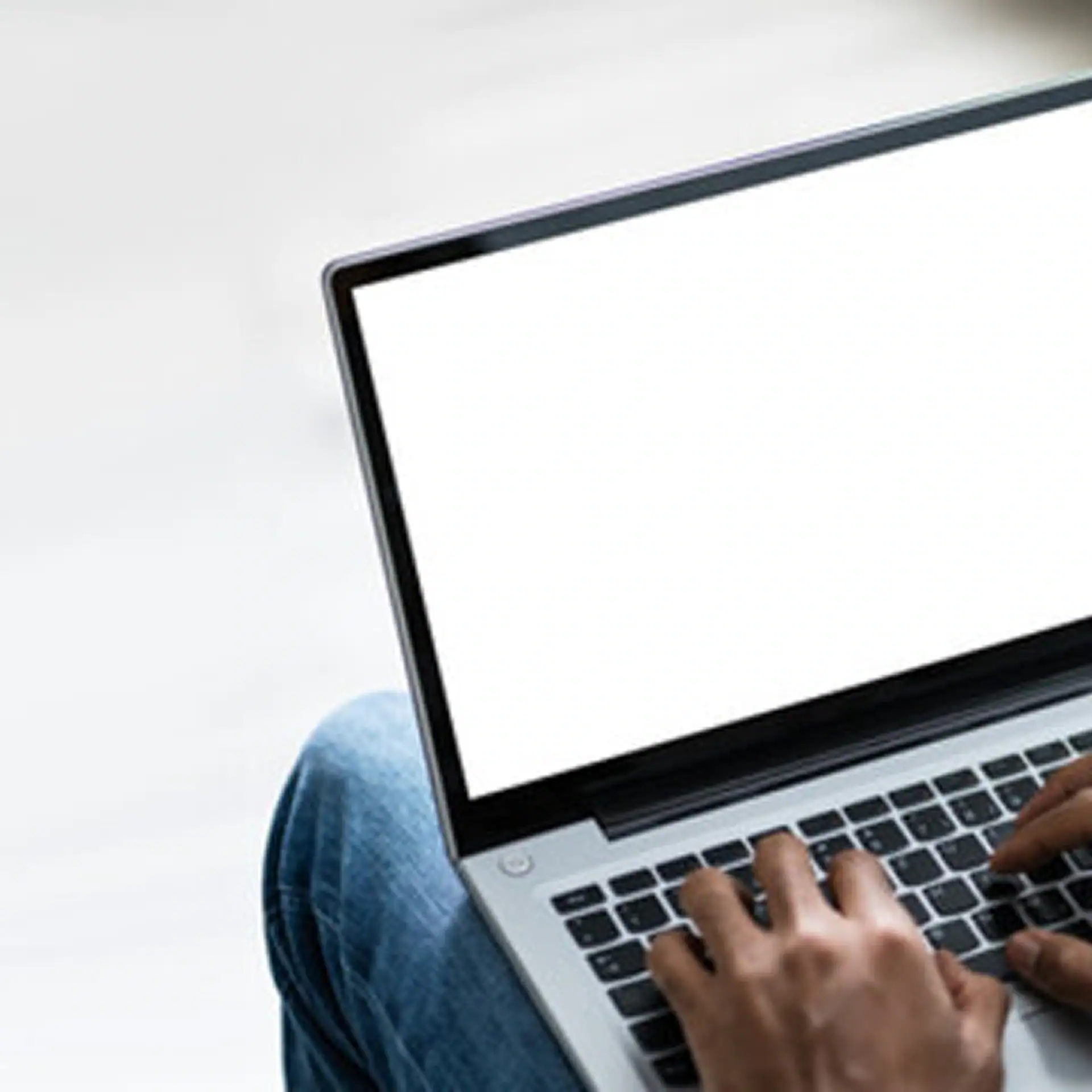 Eine Person hat einen offenen Laptop auf dem Schoß, die Finger tippen auf der Tastatur.